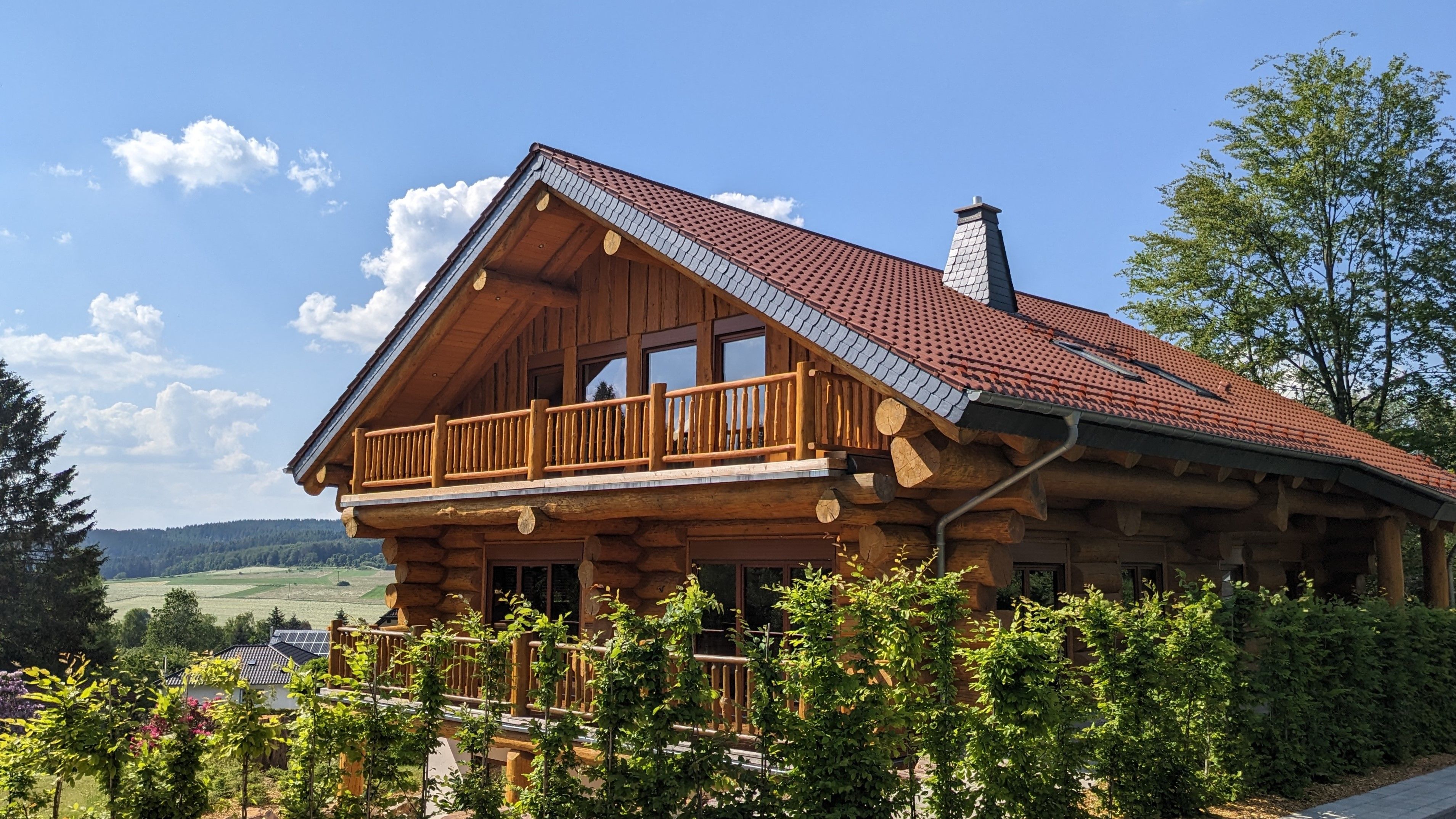 Detailaufnahme der handgefertigten Naturstamm-Fassade des Waldzeit Ferienhauses unter strahlend blauem Himmel.